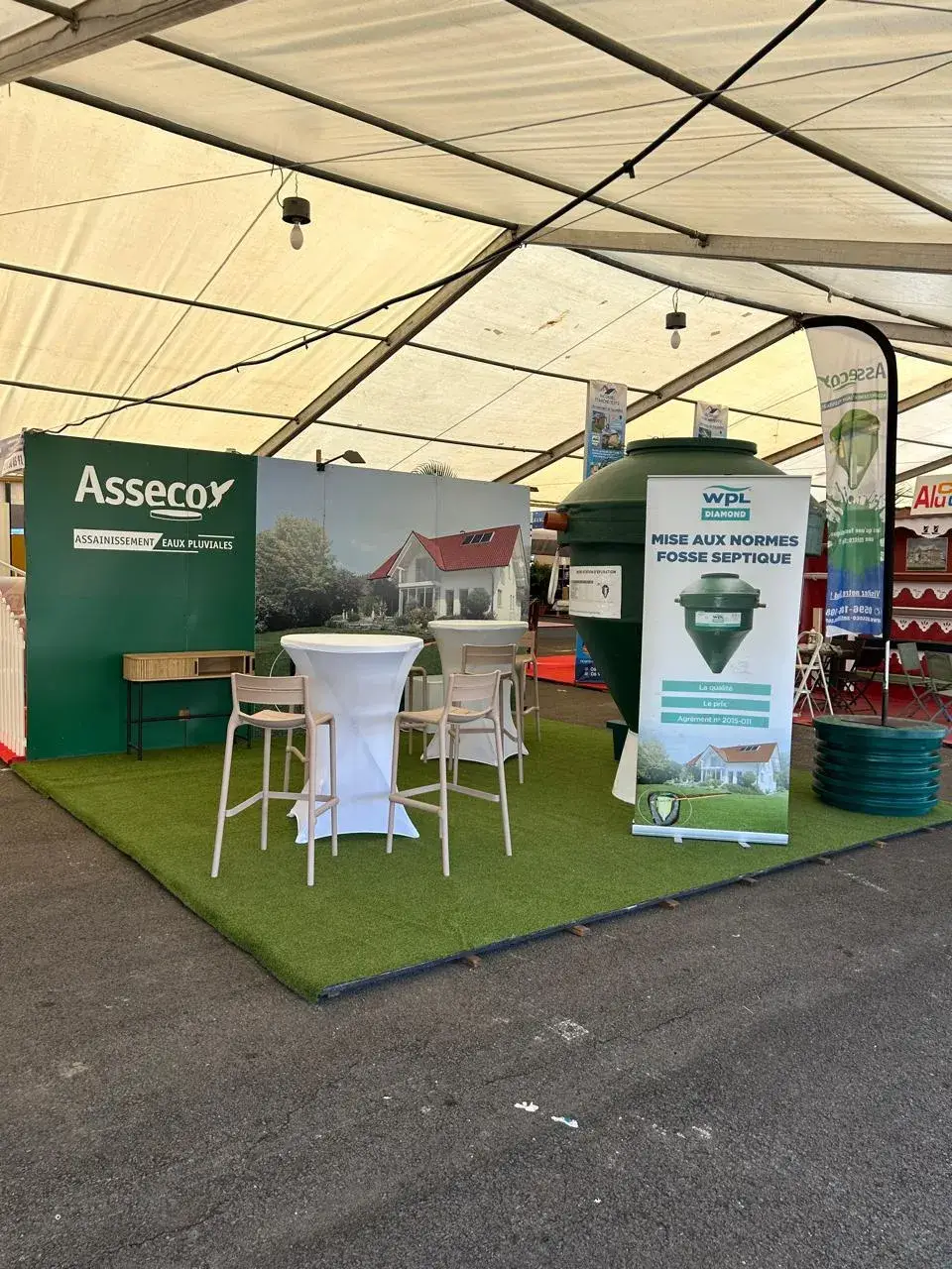 Le stand ASSECO sous un chapiteau de salon : une micro-station Diamond exposée et un kakémono « Mise aux normes fosse septique »
