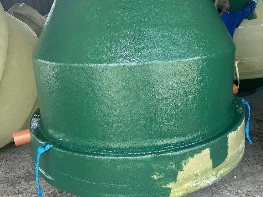Une personne, de dos, passe au rouleau le gelcoat vert sur une cuve Diamond, dans l'atelier