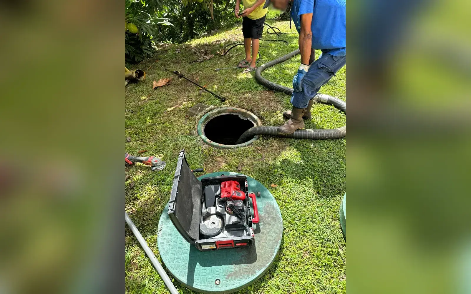 Entretien d'une micro-station dans un jardin : le tuyau d'aspiration plonge dans la cuve ouverte, une caisse à outils est posée sur son couvercle
