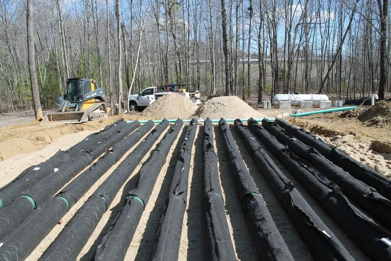 Grand chantier Enviro-Septic : une douzaine de rangées de conduites noires posées côte à côte sur un lit de sable, avant remblai