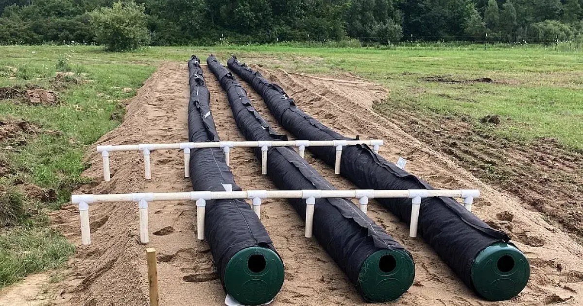 Filtre Enviro-Septic d'une maison avant remblai : trois rangées de conduites noires sur un lit de sable, reliées par des tuyaux de ventilation blancs