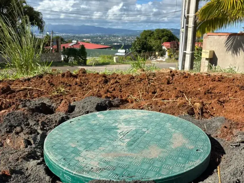 Couvercle vert d'une cuve tout juste posée dans la terre rouge, vue sur la baie et les mornes en arrière-plan