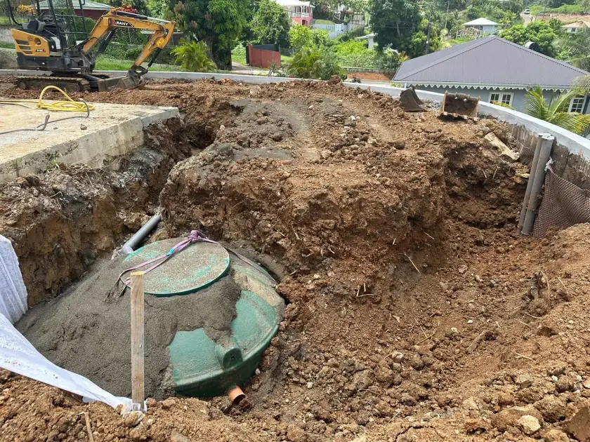 Une cuve verte calée au sable au fond de sa fouille, à côté d'une piscine en construction