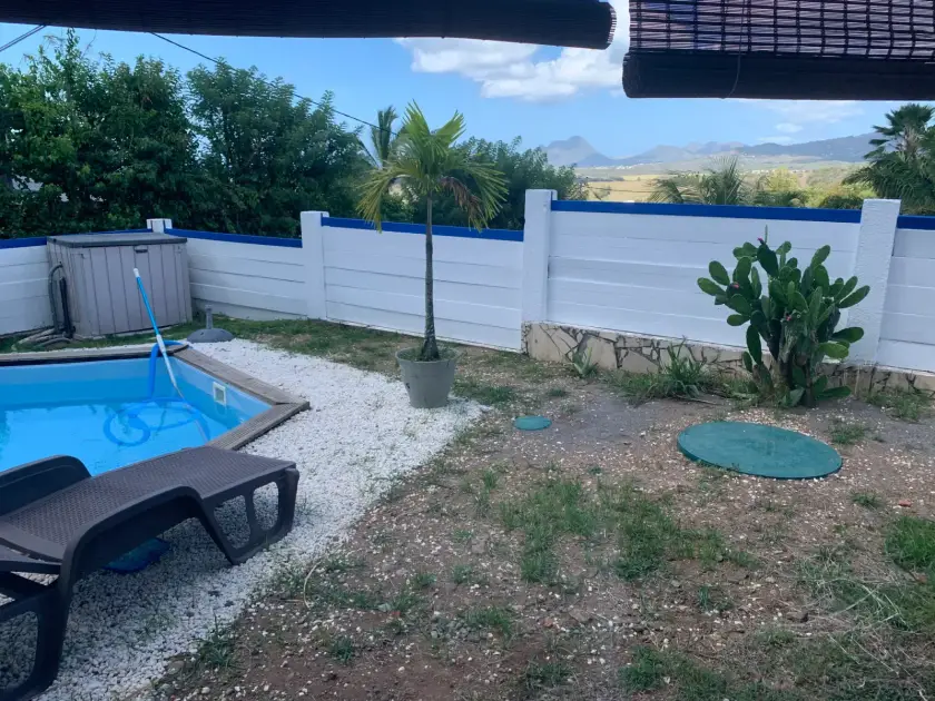 Jardin clôturé avec piscine, deux couvercles verts de cuve enterrée dans la terre, montagnes au loin