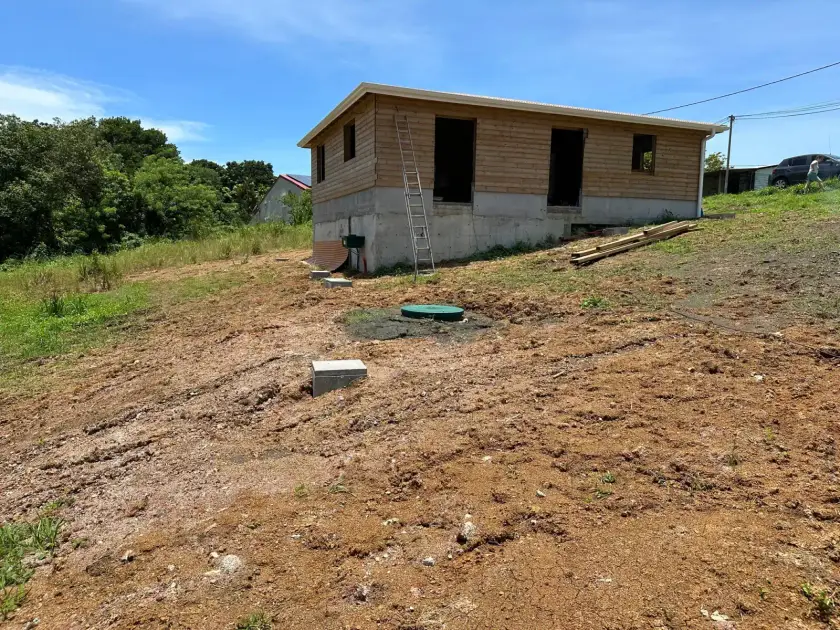 Maison en bois en construction sur un terrain terrassé, couvercle vert d'une cuve au premier plan