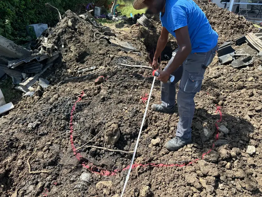 Un poseur en chapeau de paille mesure au mètre ruban l'emplacement de la cuve, tracé à la peinture rouge