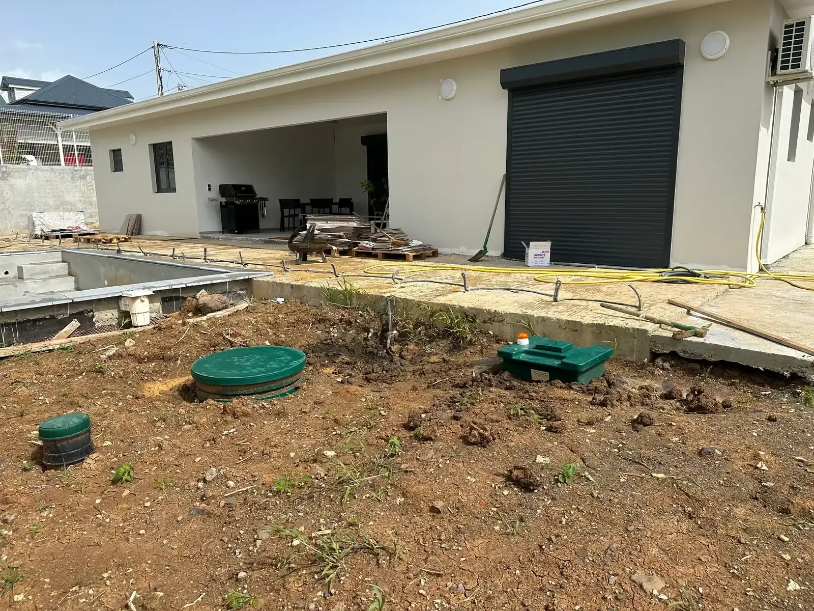 La même maison terminée, terrain remblayé devant la piscine, deux couvercles verts au ras du sol