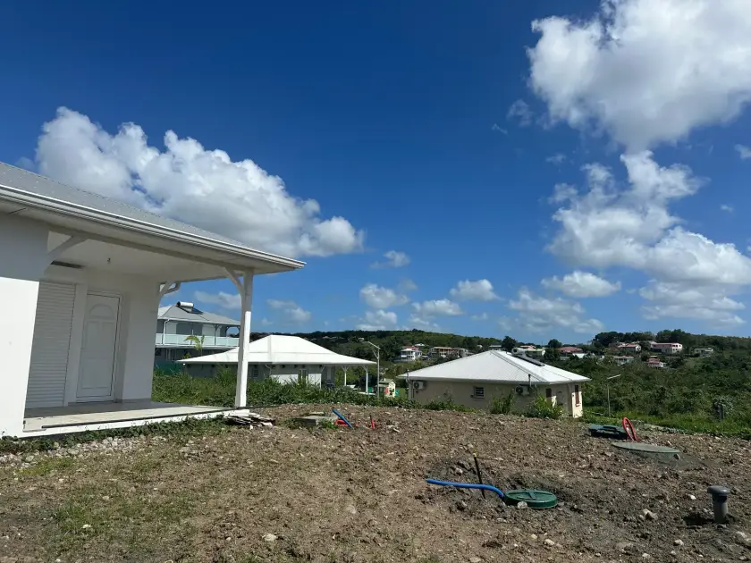 Maison blanche de plain-pied sur un terrain nivelé, couvercles de l'installation au ras du sol, vue sur les mornes