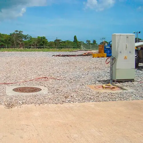 Station AQUAMAX enterrée à Trinidad : deux tampons au sol et l'armoire de commande, sur un terrain en climat tropical