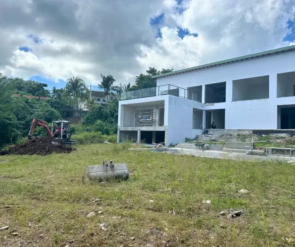 Terrain en herbe devant une maison en construction, avant les travaux ; une mini-pelle attend au fond